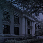 Dark blue and purple tinted image of a two-story stone building with large windows and four pillars framing the entrance